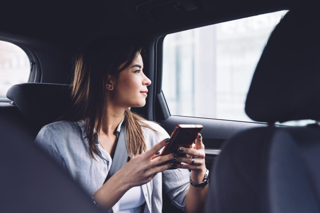 Young content woman with smartphone in car backseat