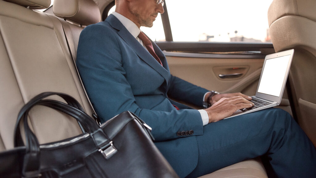 Busy businessman. Cropped photo of a man in full suit working on his laptop while sitting in the car